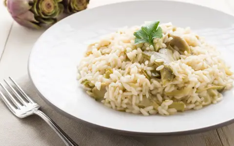 Un cremoso risotto con carciofi freschi, guarnito con un ciuffo di prezzemolo, pronto per essere gustato.