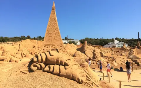 Beeindruckende Sandskulpturen, darunter der Eiffelturm, im Sand City Algarve. Besucher bestaunen die Kunstwerke.