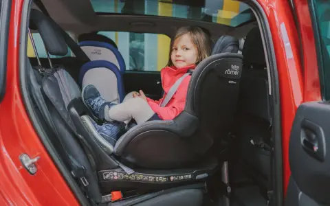Mała dziewczynka w czerwonej kurtce siedzi w foteliku samochodowym Britax Römer.