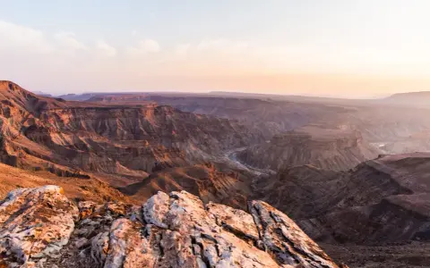 Wąwóz Fish River w Namibii, z rzeką wijącą się w dole. Zachodzące słońce maluje skały na ciepłe barwy.