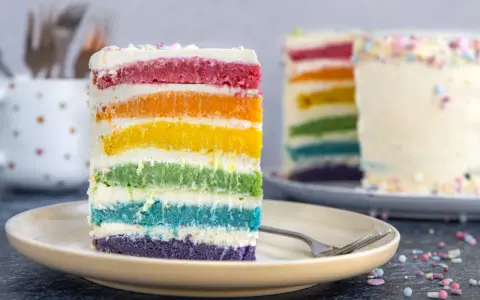 Ein Stück Regenbogen Kuchen mit bunten Schichten und Streuseln auf einem Teller.