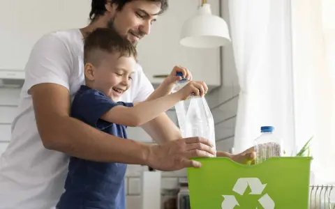 Padre e hijo reciclando botellas de plástico en un contenedor verde. Enseñando conciencia ecológica desde pequeños.