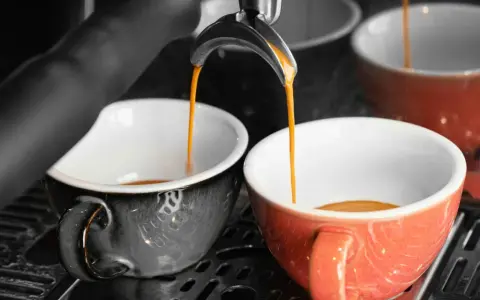 Dwie filiżanki, jedna szara, druga pomarańczowa, napełniają się aromatyczną kawą doppio.