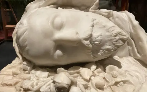 Sculpture en marbre d'un visage endormi, entouré de fleurs. Une œuvre d'art évoquant la célèbre Sarah Bernhardt.