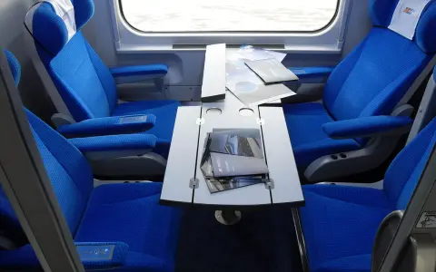 Wnętrze wagonu przedziałowego z wygodnymi, niebieskimi fotelami i stolikiem.