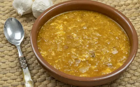 Sopa de ajo tradicional en cuenco de barro, con ajos y cuchara al lado.