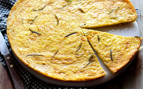Una torta dorata, profumata al rosmarino, perfetta come ricetta con farina di ceci. Una fetta è già stata tagliata.
