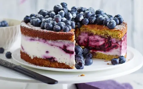 Saftige Heidelbeertorte mit Joghurt-Füllung, garniert mit frischen Beeren und Puderzucker. Ein Genuss für Augen und Gaumen.