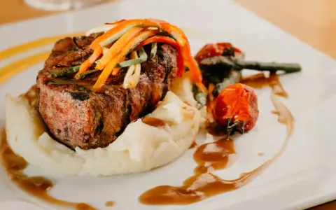 Un plat de viande grillée, purée de pommes de terre et légumes, une des spécialités d'Aurillac, servi sur une assiette blanche avec une sauce brune.