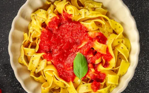 Pappardelle z sosem pomidorowym i bazylią, klasyczne makaron po włosku, podane w kremowej misce.