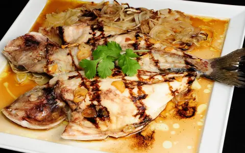 Dorada a la espalda, a la parrilla, con láminas de ajo y cebolla caramelizada, servida en salsa dorada.