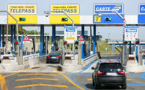 Casello autostradale con corsie Telepass e carte. Un'auto nera attende, forse per un mancato pagamento Telepass senza ricevuta.