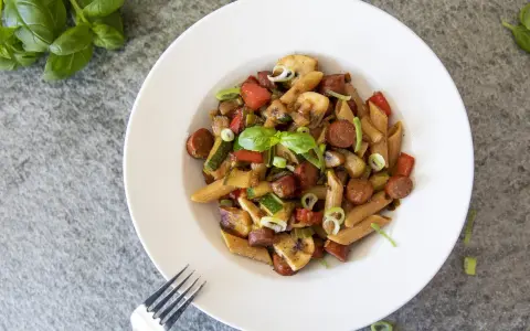 En tallrik med chorizo pasta med grönsaker som paprika, zucchini och champinjoner. Garnerad med färsk basilika och salladslök.
