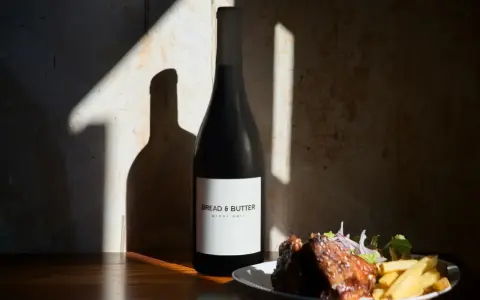 En flaska Bread & Butter Pinot Noir står bredvid en tallrik med revbensspjäll och pommes frites. Perfekt för en mysig kväll.
