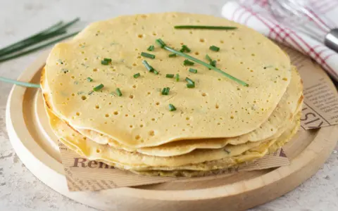 Pila di piadine di ceci dorate, guarnite con erba cipollina fresca. Perfette per un pasto leggero e gustoso.
