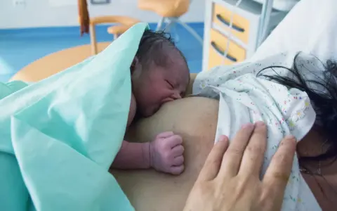 Neugeborenes Baby an der Brust der Mutter, ein Moment der stillen Geburt und des ersten Kontakts.