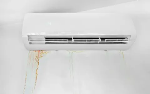 Condizionatore bianco con macchie d'acqua sul muro. La condensa gocciola, creando aloni color ruggine e verdognoli.