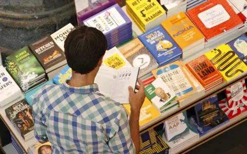 Hombre en una librería, rodeado de libros sobre finanzas y negocios, buscando las mejores editoriales para publicar un libro.