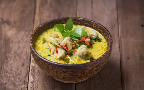 Zielone curry z kurczakiem i chili w drewnianej misce na desce.