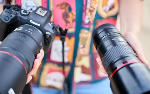 Dwie ręce trzymają obiektywy do Canona. Jeden z nich to Canon RF 135mm f/1.8L IS USM, drugi to Canon EF 135mm f/2L USM.