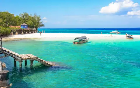 Zanzibar - wczasy opinie: turkusowa woda, biała plaża, drewniany pomost i łodzie. Rajskie widoki idealne na wakacje.