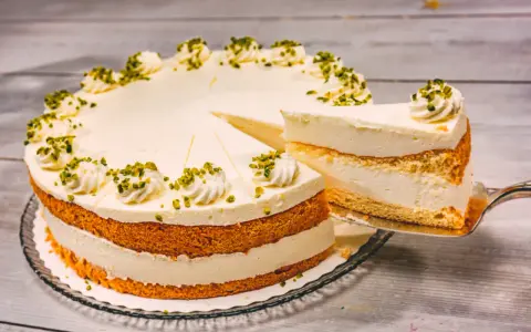 Eine Buttermilch Zitronen Torte mit cremiger Füllung und Pistazien-Deko. Ein Stück wird gerade herausgeschnitten.