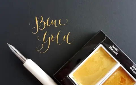 Złoty napis "Blue Gold" obok pióra i palety farb.