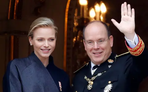 Charlene, furstinna av Monaco, ler vid sidan av prins Albert. Han vinkar glatt till publiken.