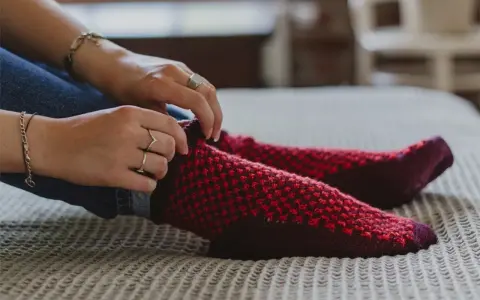 Manos ajustando calcetines rojos y morados tejidos a mano con agujas circulares.