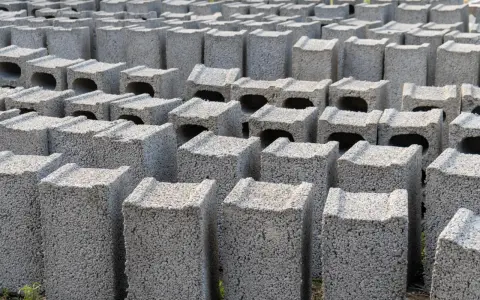 Rzędy betonowych bloczków, gotowych na fundamenty. Wybór między bloczkami z betonu a wylewanymi fundamentami jest kluczowy dla trwałości budowli.