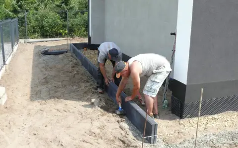 Dwóch mężczyzn układa obrzeża pod kostkę. Suchy beton pod kostkę jest przygotowywany do dalszych prac.