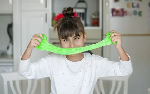 Bambina sorridente con slime verde brillante, un divertente esperimento per la ricetta slime fatta in casa.