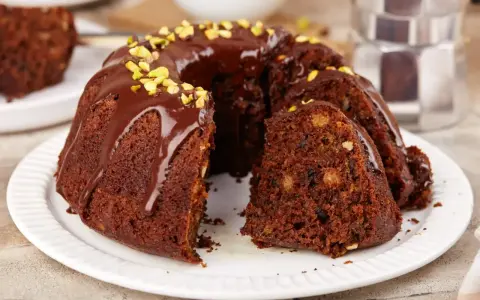 Pyszna babka na oleju, polana czekoladą i posypana pistacjami, z kawałkiem na talerzyku.