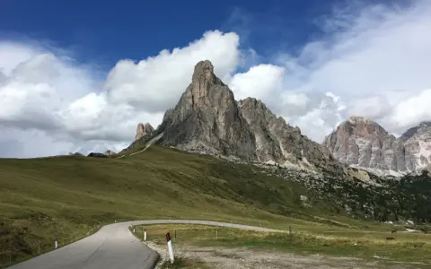 Strada tortuosa verso le Dolomiti, perfetta per una gita in moto. Montagne imponenti e cielo azzurro con nuvole bianche.