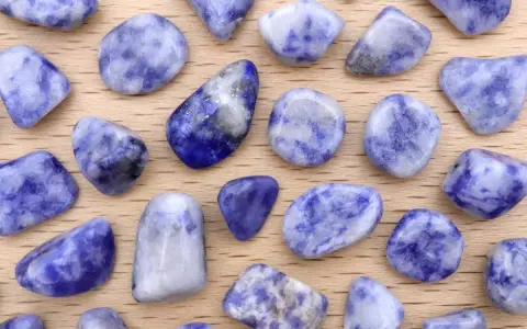 Tumbled sodalite stones, showcasing their deep blue and white patterns. Le pietre di sodalite, con le loro proprietà calmanti, sono disposte su un fondo di legno.
