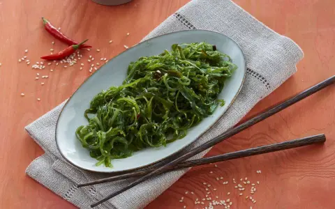 Ein Teller mit leckerem Wakame Salat, garniert mit Chilis und Sesam. Dazu liegen Holzstäbchen bereit.