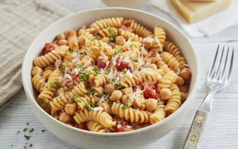 Eine Schüssel Fusilli-Nudeln mit Kichererbsen, Tomaten und Parmesan, garniert mit Petersilie.