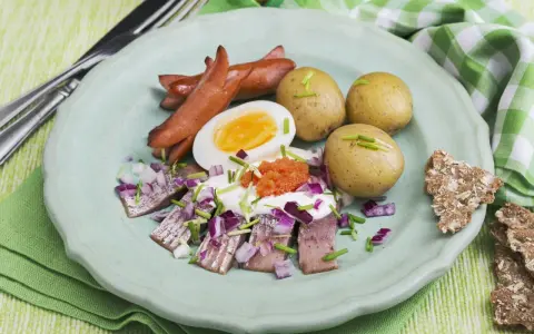 En tallrik med sill, ägg, korv och potatis. En klassisk del av ett svenskt påskbord med mat som passar alla.
