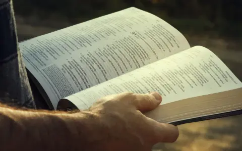 A hand holds open a Bible, revealing the words of Agur in the Bible, Proverbs 31:2.