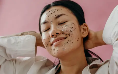 Une jeune femme au visage couvert d'un masque exfoliant scintillant, profitant d'un moment de détente. Elle nous rappelle pourquoi exfolier sa peau est essentiel pour un teint éclatant.