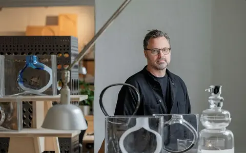 Matti Klenell, en man med glasögon, står bland sina konstverk av glas.