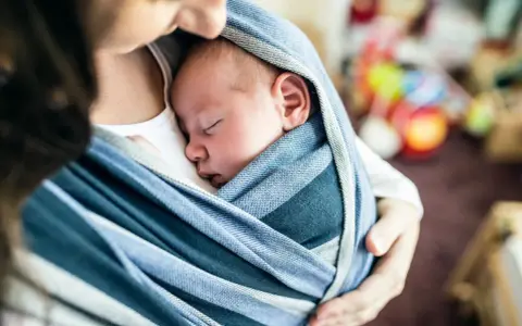 Ein Baby schläft friedlich in einem blauen Tragetuch. Der sanfte Tagesrhythmus des Babys wird durch die Nähe zur Mutter unterstützt.
