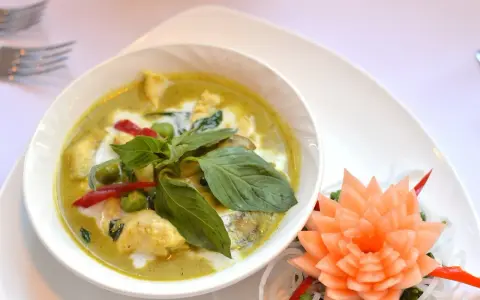 Zielone curry z kurczakiem, ozdobione bazylią i kwiatkiem z marchewki.