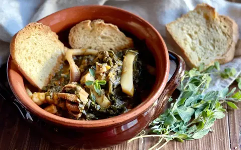 Seppie in zimino, un piatto tradizionale con seppie tenere e verdure, servito in una ciotola di terracotta con pane tostato e erbe aromatiche.