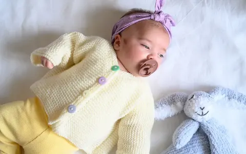 Un bebé con un suéter tejido a dos agujas y un conejito de peluche. El suéter es un muestrario de puntos a dos agujas para bebes.