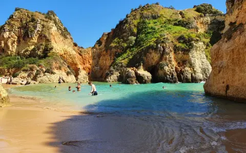 Sonnige Bucht mit Felsen und türkisfarbenem Wasser. Menschen baden und genießen das milde Wetter im **Portugal im Dezember**.
