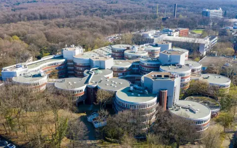 Luftaufnahme des Campus der **Uni Duisburg Essen** mit seinen charakteristischen runden Gebäuden, umgeben von Bäumen.