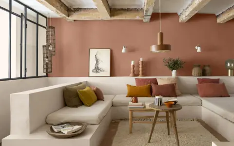 Salon cosy aux murs couleur brun terre de France, banquette en L, coussins ocre et rouille, table basse en bois brut.