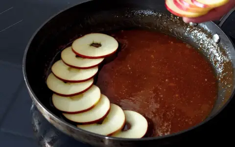 Äppelringar läggs i en panna med karamelliserad sås, förberedelse för en klassisk tarte tatin.