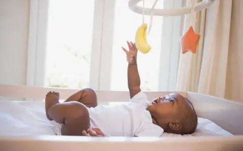 Maluch wyciąga rączkę do bananka i gwiazdki wiszących na karuzeli do łóżeczka.